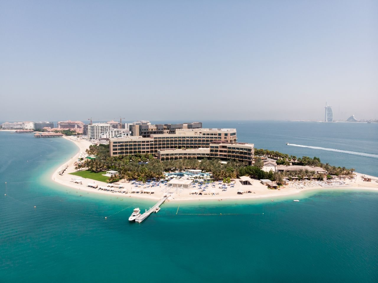 our-story-02 Stunning aerial shot of a luxury hotel on Dubais Palm Jumeirah island, surrounded by turquoise waters.